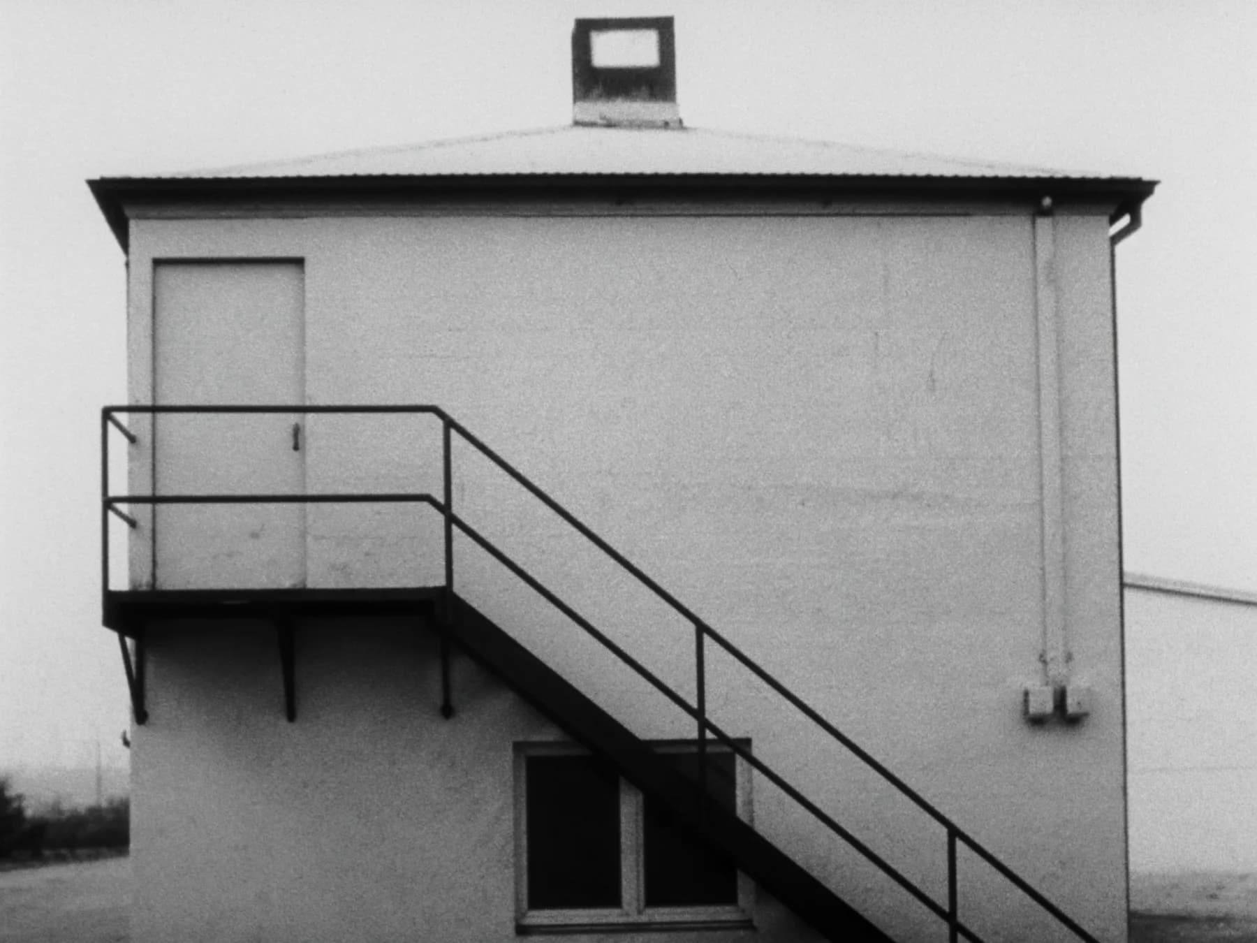 An external fire-escape stair on a blank concrete wall, leading to a roof hatch